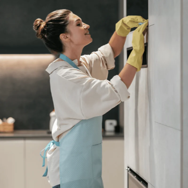 House cleaner wiping kitchen appliance and cabinets.